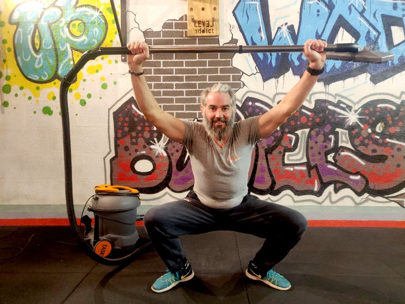 Homme avec un aspirateur en position overhead squat